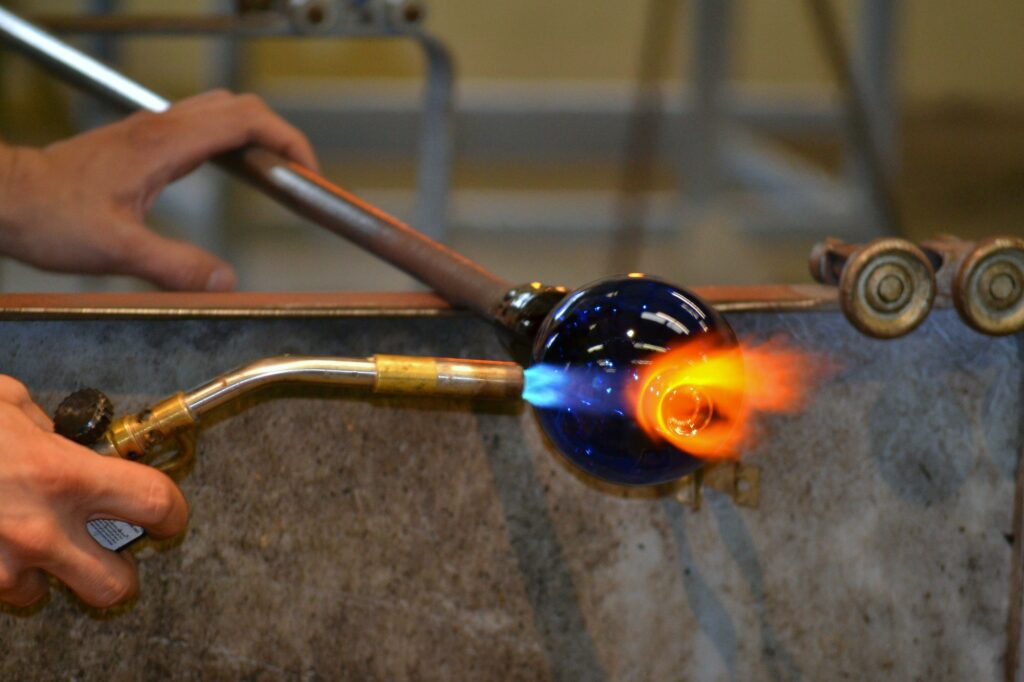 man male artisan person using a blowtorch on a hand crafted goblet in a glass blowing studio